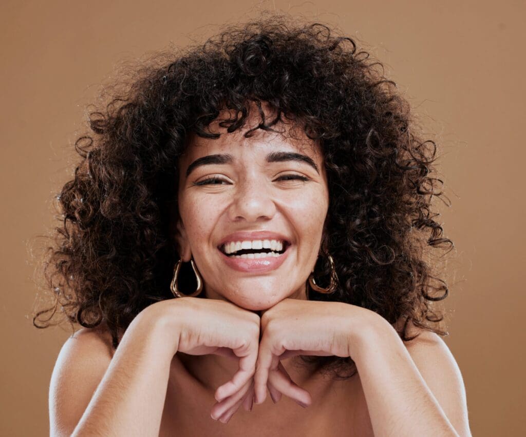 black woman in studio with natural hair wearing gold earrings and a big smile